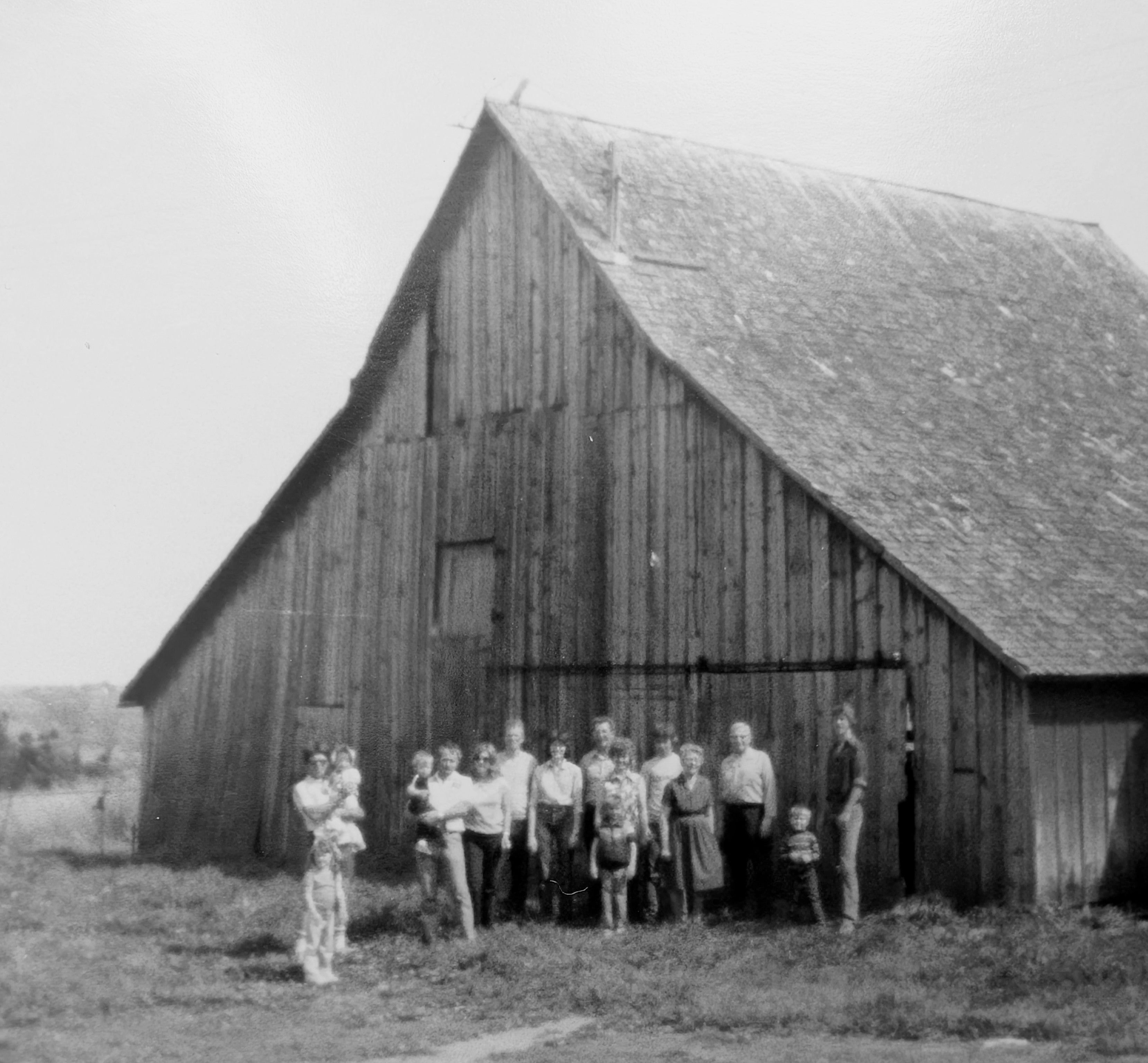 Black and white image of a family standing near a barn, representing family, continuity, and generational heritage.