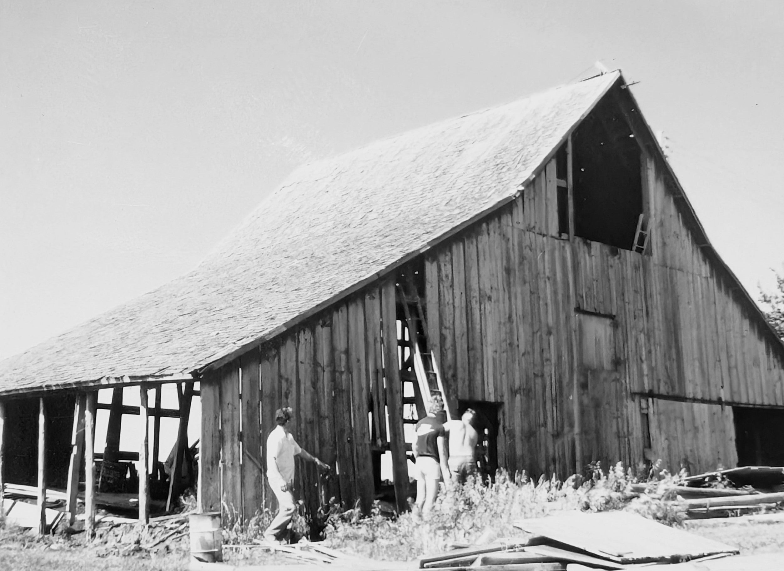 Black and white image of three men repairing a barn, reflecting hard work, craftsmanship, and shared responsibility.